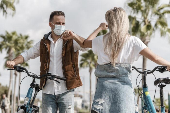 homem e mulher com máscara se cumprimentam com o cotovelo. Eles estão de bicicleta.